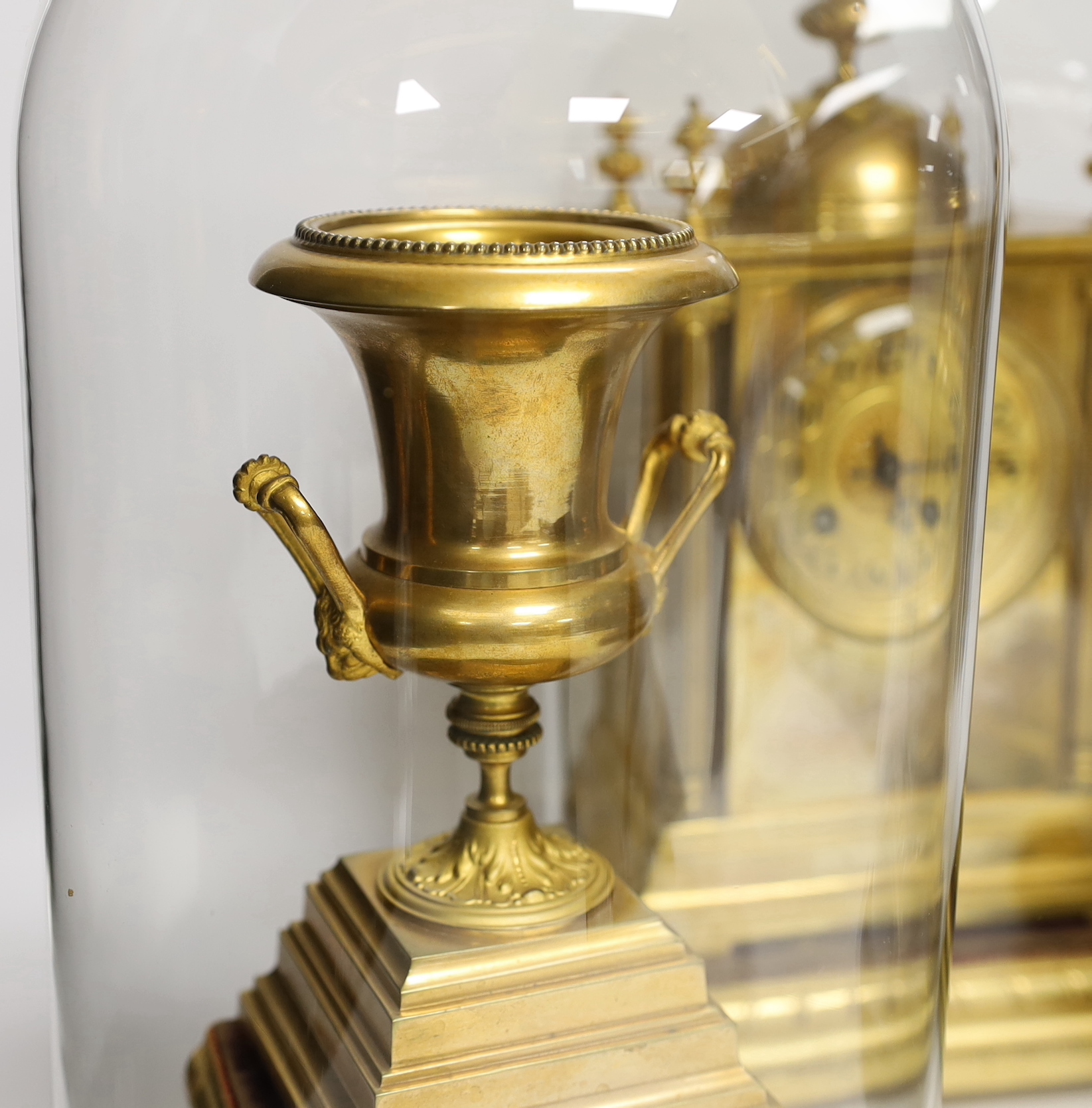 A gilt metal clock garniture, c.1900, with a pair of urns, all under glass domes, French movement by A D Mougin, striking on a gong, (missing base for clock dome), 36cm high